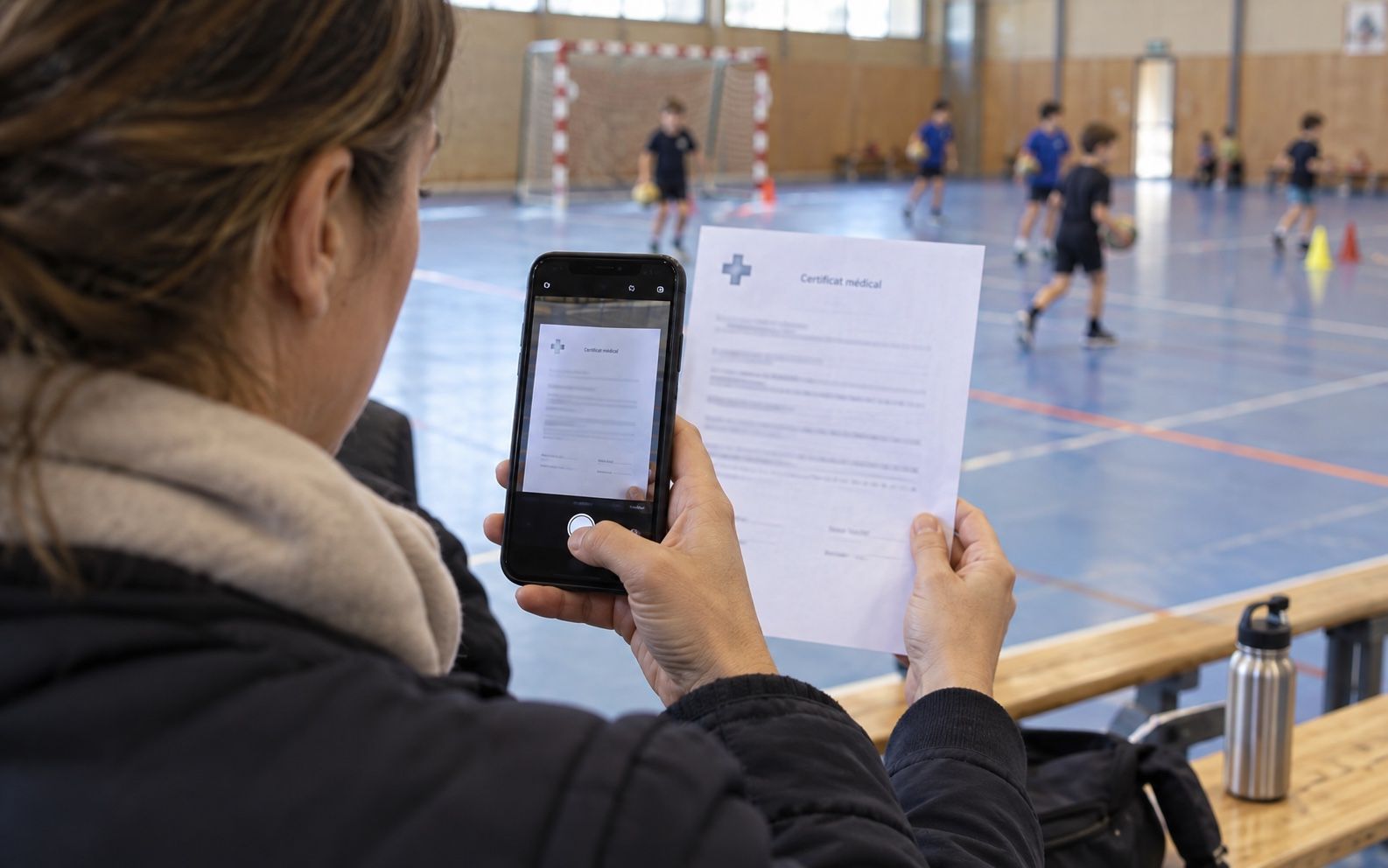 Parent photographing the medical certificate with a smartphone at the side of the sports hall to upload it