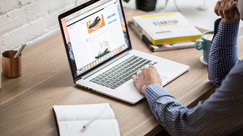 Portátil sobre un escritorio con una página web abierta y una libreta al lado